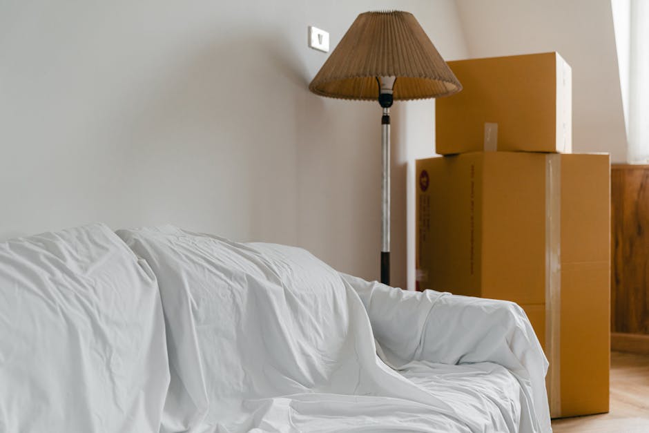 Photograph of a home relocation scene showing a corridor or hallway inside a property with several cardboard moving boxes stacked on a trolley, ready for transport. The boxes vary in size and are seal
